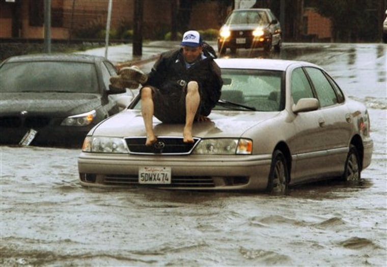 A man gets ready to jump off the hood of his car, stalled on flooded Vineland Ave between Vanowen and Sherman Way, in the North Hollywood area of Los Angeles' San Fernando Valley Sunday, March 20, 2011.  The first day of spring arrived with a bang in Southern California, bringing heavy snow to the mountains and illuminating the sky with flashes of lightning from Santa Barbara to downtown Los Angeles. (AP Photo/Mike Meadows)